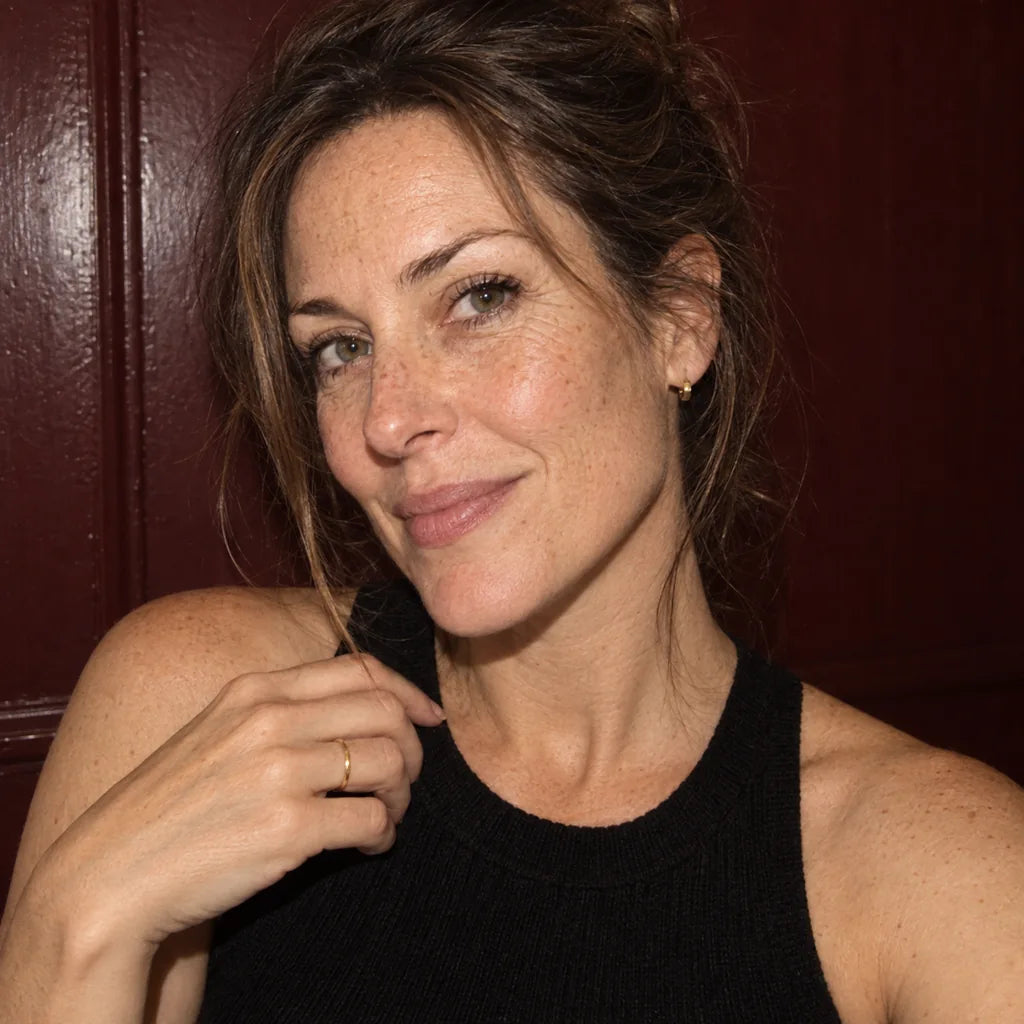 Candid-style illustrative portrait of a woman with freckles, loosely tied hair and a black knit top. Not a customer result.