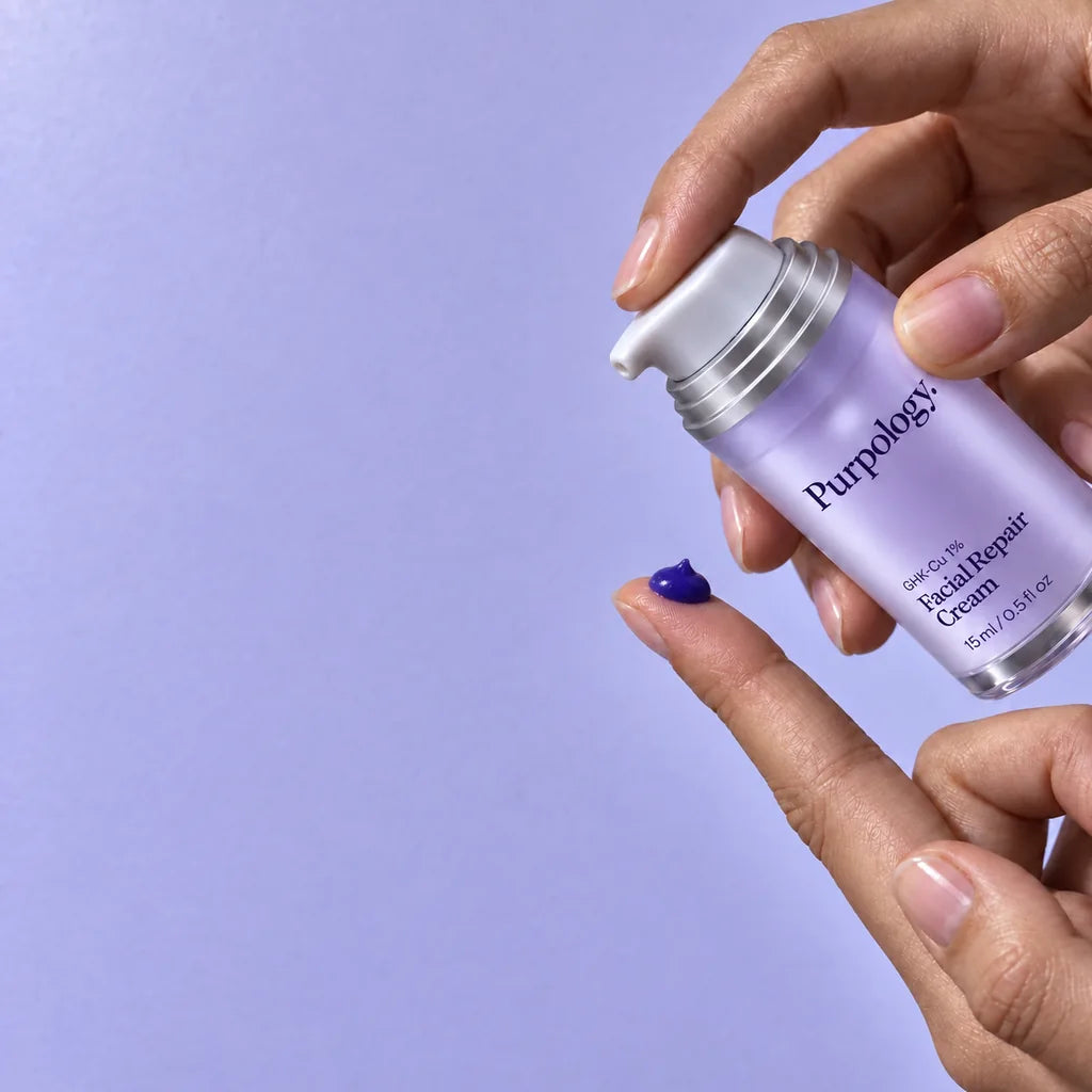 A large pea-sized amount of rich violet cream on a fingertip beneath the lavender Purpology pump.
